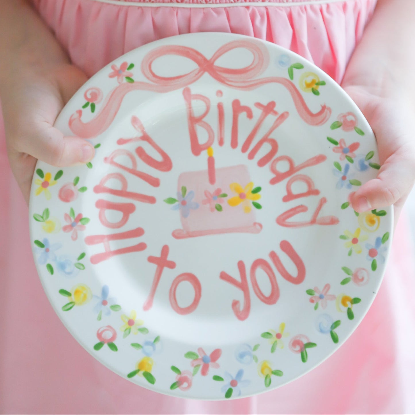 Child holding a 'Happy Birthday to you' plate with a pink dress.