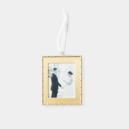 A rectangular gold picture frame ornament with a white hanging ribbon, featuring a black-and-white wedding photo of a couple, shown against a light gray background.