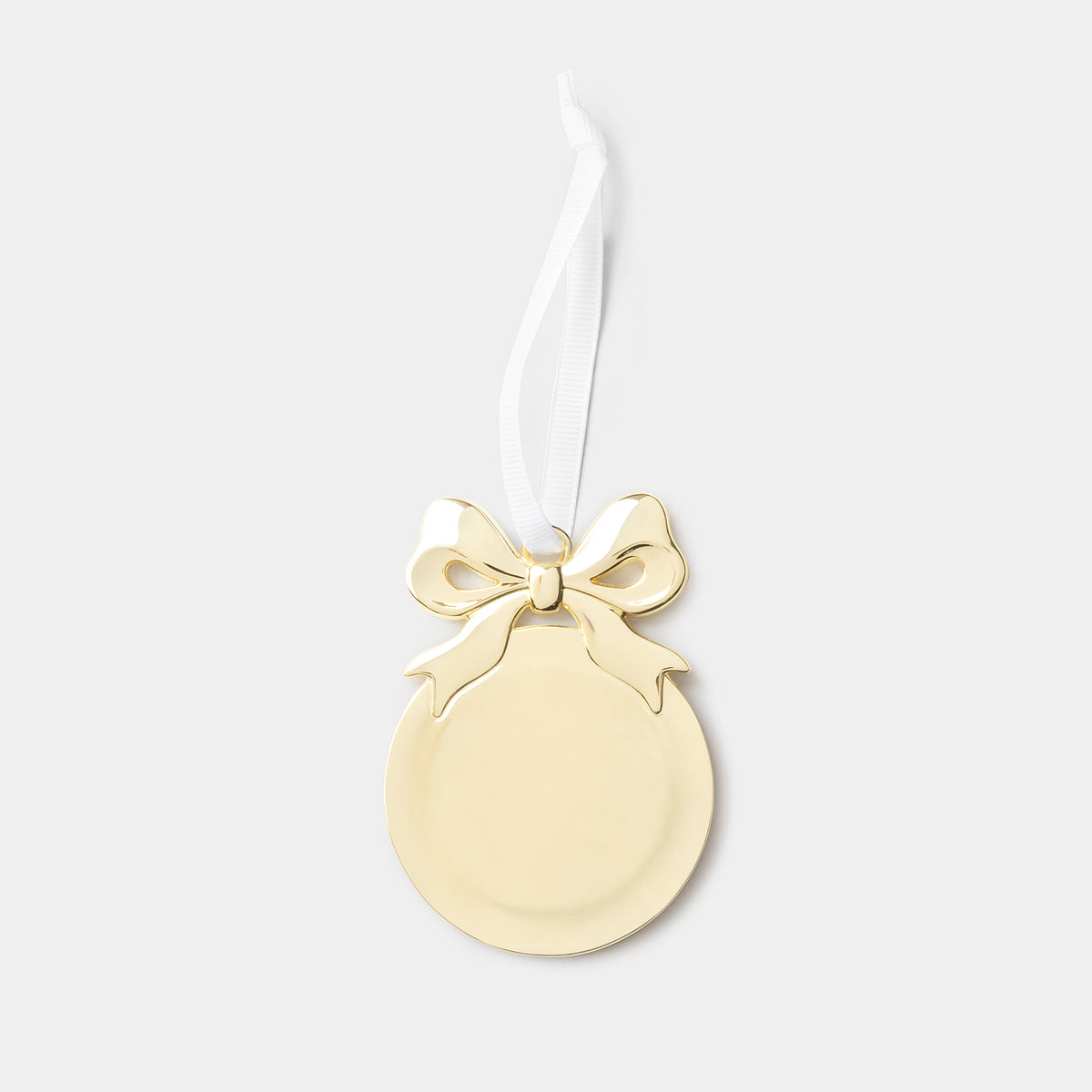 A gold oval Christmas ornament with a bow detail and a white hanging ribbon, shown against a light gray background.