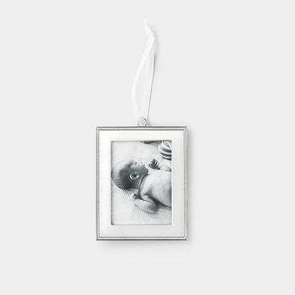 A rectangular silver picture frame ornament with a beaded border and a hanging white ribbon, shown against a light gray background. The photo insert inside the frame is a black-and-white image of a baby.